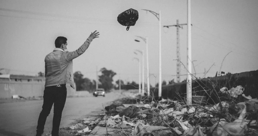 A man is throwing a garbage bag into a trash area.