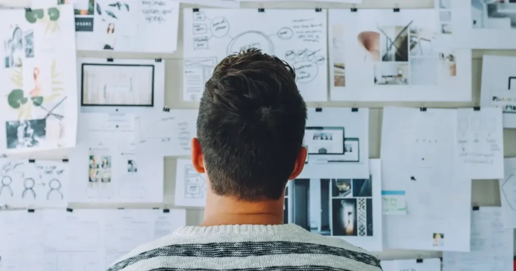 A man is staring at a whiteboard, thinking about his plan.