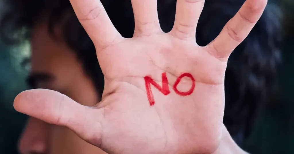 A man with the word "NO" written on his palm is pointing his hand towards me in refusal.