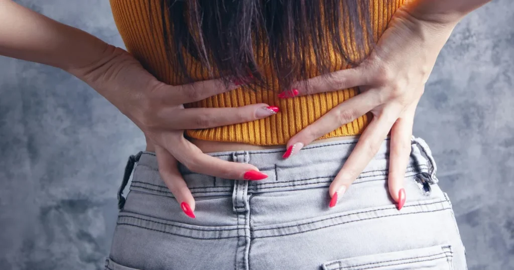 A person holding their hand in pain on their lower back.